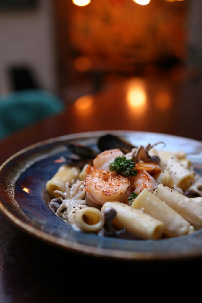 Close-up of seafood rigatoni pasta with shrimp and mushrooms in warm lighting.