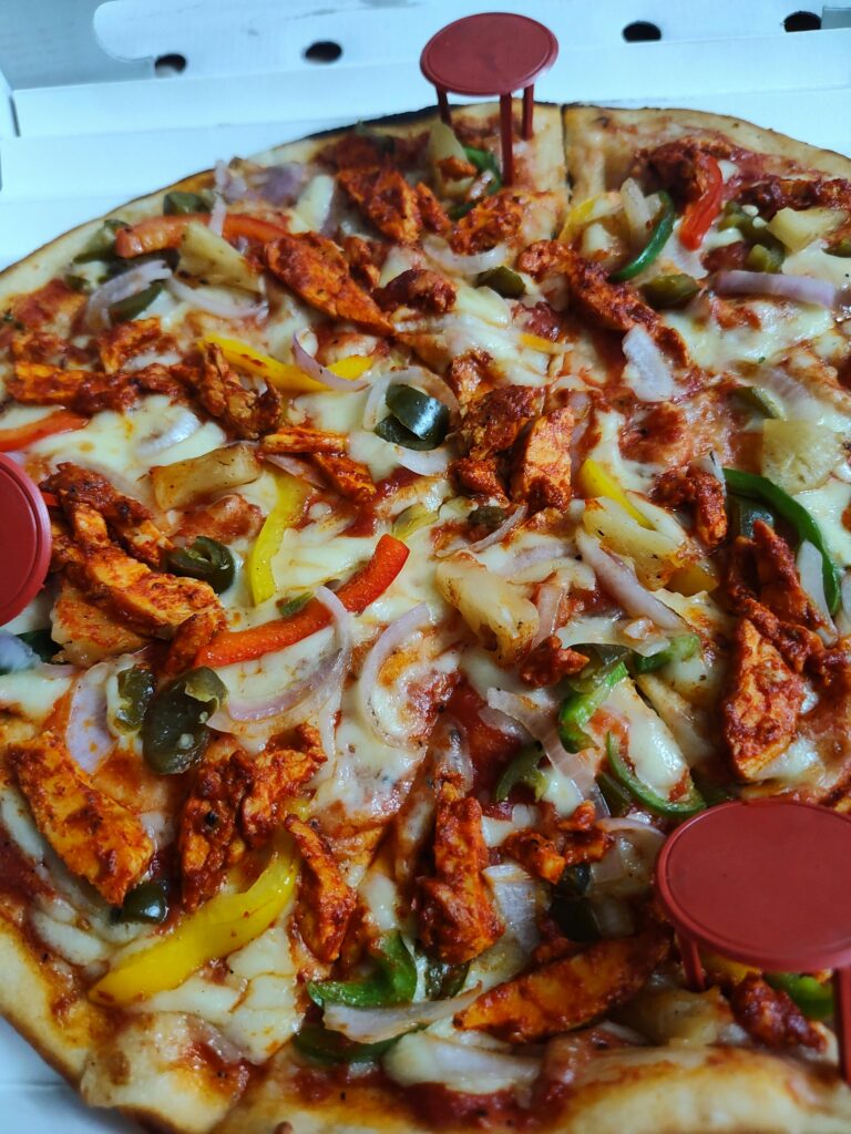 Delicious spicy chicken pizza topped with colorful peppers and melted cheese in a pizza box.
