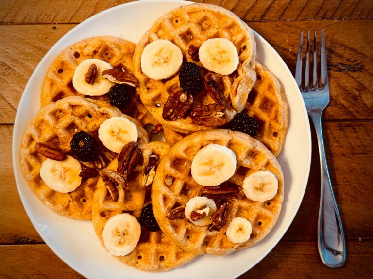 Mouthwatering waffles topped with banana slices, pecans, and blackberries on a rustic wooden table.